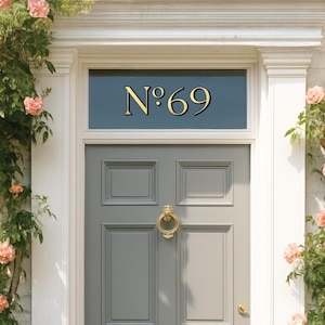 May include: A gray front door with a gold door knocker and the number "N&deg;69" in gold lettering above. The door is surrounded by white trim and flowering vines.