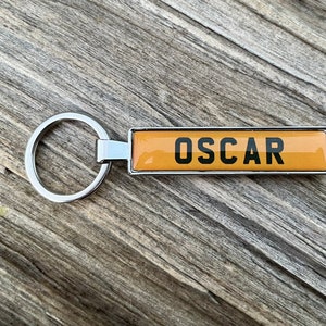 May include: A silver keychain with a yellow rectangular tag that says "OSCAR" in black letters.