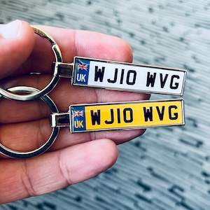 May include: Two silver keyrings with a UK flag charm. The keyring charms are shaped like number plates with the text "WJIO WVG" in black letters. One number plate is white and the other is yellow.