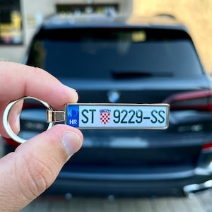 Op de afbeelding: Een zilveren sleutelhanger met een replica van een Kroatisch kenteken in blauw en wit. De kentekenplaat heeft de tekst "ST 9229-SS HR".