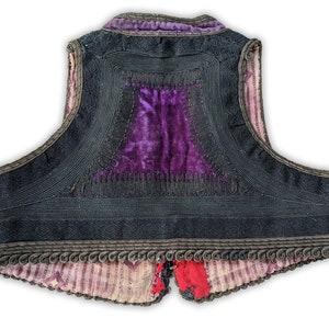 Puede incluir: Un chaleco vintage con exterior negro, con intrincados ribetes de cord&oacute;n y un panel central de terciopelo morado vibrante. Los bordes del chaleco est&aacute;n adornados con adornos decorativos, y el forro muestra un patr&oacute;n de rayas.