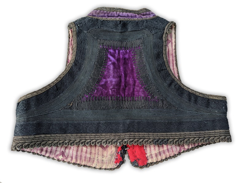 Puede incluir: Un chaleco vintage con exterior negro, con intrincados ribetes de cord&oacute;n y un panel central de terciopelo morado vibrante. Los bordes del chaleco est&aacute;n adornados con adornos decorativos, y el forro muestra un patr&oacute;n de rayas.