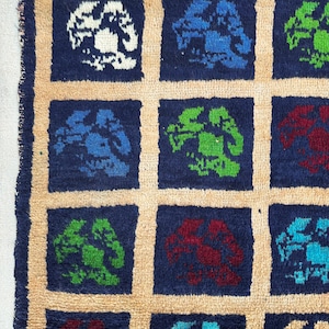 May include: A close-up of a blue rug with a repeating pattern of stylized trees in various colors, including white, blue, green, and red.