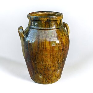 May include: A large, brown ceramic jar with two handles. The jar has a glazed finish and is decorated with a pattern of lines and dots.