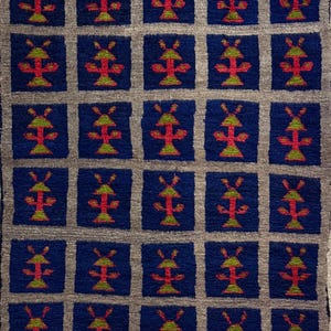 Könnte beinhalten: Ein rechteckiger Teppich mit einem sich wiederholenden Muster aus blauen Quadraten mit einem rot-grünen Design, vor einem grauen Hintergrund. Der Teppich hat einen Fransenbesatz entlang der Unterkante. Das Design ist symmetrisch und geometrisch.