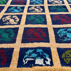 May include: A blue and beige rug with a repeating pattern of colorful stylized trees. The rug has a fringe border.