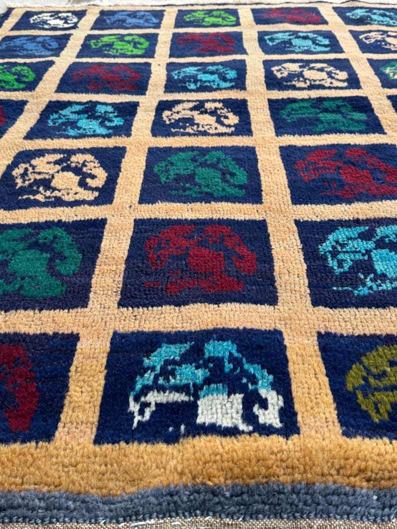 May include: A blue and beige rug with a repeating pattern of colorful stylized trees. The rug has a fringe border.