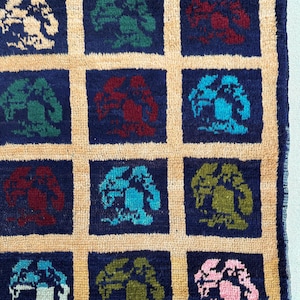 May include: A close-up of a rug with a repeating pattern of stylized trees in various colors, including blue, green, red, and pink. The trees are set against a dark blue background and are surrounded by a light beige border.