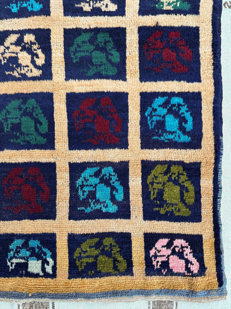 May include: A close-up of a rug with a repeating pattern of stylized trees in various colors, including blue, green, red, and pink. The trees are set against a dark blue background and are surrounded by a light beige border.