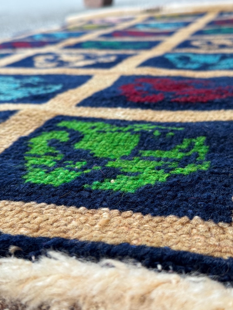 May include: Close-up of a blue and beige patterned rug with green, red, and blue squares. The rug has a fringe border.