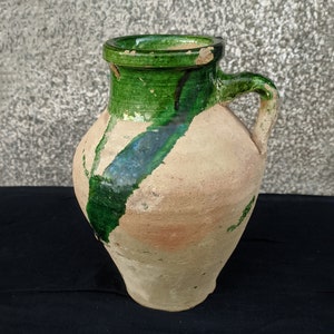 Può includere: Un'anfora in ceramica marrone con una glassa verde. L'anfora ha un manico e una bocca larga.