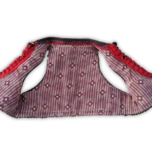 Puede incluir: Un chaleco vintage con ribete rojo y negro. El interior presenta un patr&oacute;n de rayas moradas y blancas con detalles de diamantes. Los bordes del chaleco est&aacute;n adornados con elementos decorativos negros y rojos.