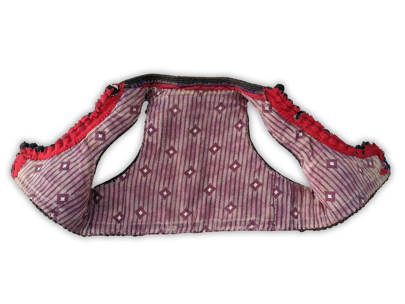Puede incluir: Un chaleco vintage con ribete rojo y negro. El interior presenta un patr&oacute;n de rayas moradas y blancas con detalles de diamantes. Los bordes del chaleco est&aacute;n adornados con elementos decorativos negros y rojos.