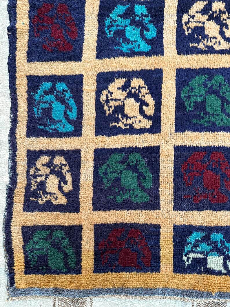 May include: A colorful rug with a repeating pattern of stylized trees in shades of blue, green, red, and white. The trees are set against a dark blue background and are surrounded by a light beige border.