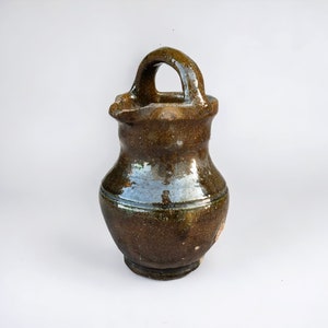 May include: A brown ceramic pitcher with a handle. The pitcher has a green glaze and is slightly chipped.