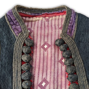 Puede incluir: Un chaleco vintage con un dise&ntilde;o estampado. El chaleco presenta un exterior gris oscuro con ribetes morados y marrones. El interior tiene un patr&oacute;n de rayas rojas y blancas con formas de diamante. Tiene varios botones oscuros en forma de bola gris.