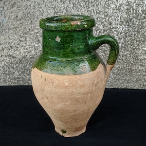 Könnte beinhalten: Ein grüner, glasierter Keramik-Krug mit einem braunen Tonkörper und einem Henkel. Der Krug hat eine breite Öffnung und einen runden Körper.