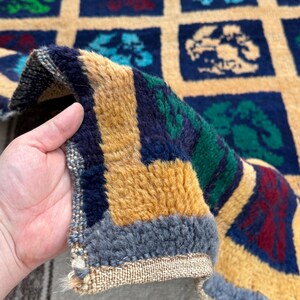 May include: Close-up of a colorful rug with a geometric pattern of squares. The rug is made of wool and has a fringe border. The rug is folded in half and the fringe is visible.