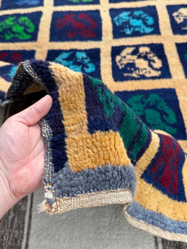May include: Close-up of a colorful rug with a geometric pattern of squares. The rug is made of wool and has a fringe border. The rug is folded in half and the fringe is visible.