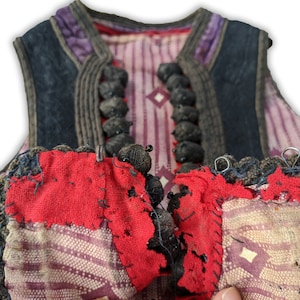 Puede incluir: Primer plano de un chaleco vintage con dise&ntilde;o de patchwork. El chaleco presenta una combinaci&oacute;n de telas rojas, moradas y estampadas. El ribete azul oscuro y los cierres de botones negros a&ntilde;aden contraste. El dise&ntilde;o del chaleco sugiere un significado hist&oacute;rico o cultural.