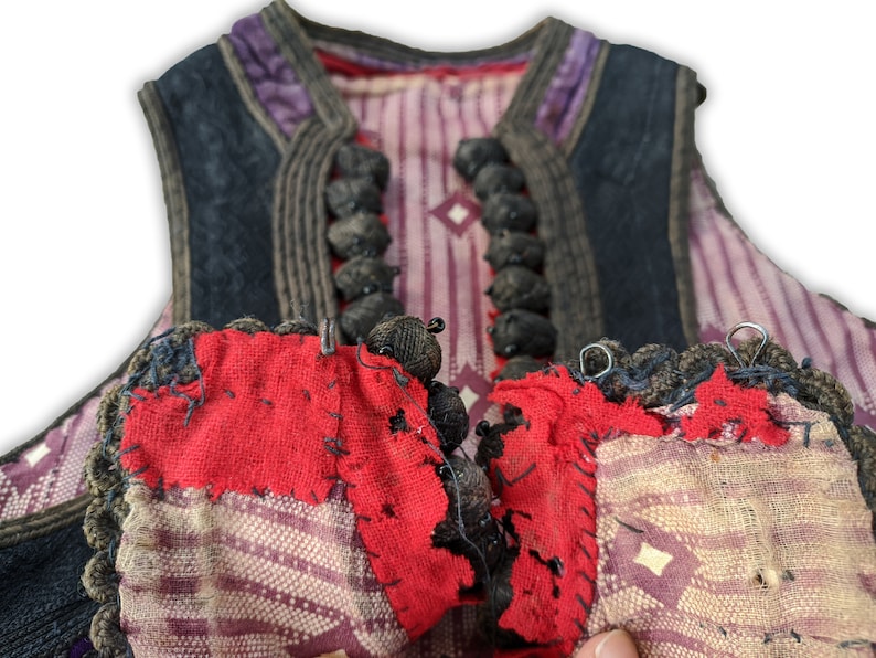 Puede incluir: Primer plano de un chaleco vintage con dise&ntilde;o de patchwork. El chaleco presenta una combinaci&oacute;n de telas rojas, moradas y estampadas. El ribete azul oscuro y los cierres de botones negros a&ntilde;aden contraste. El dise&ntilde;o del chaleco sugiere un significado hist&oacute;rico o cultural.