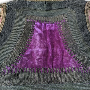 Puede incluir: Primer plano de un chaleco vintage con un panel central de terciopelo morado. El chaleco est&aacute; adornado con cord&oacute;n negro y costuras decorativas. Los bordes est&aacute;n forrados con una tela estampada.