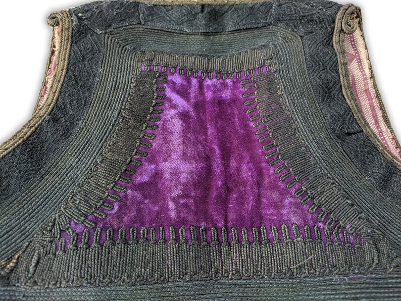 Puede incluir: Primer plano de un chaleco vintage con un panel central de terciopelo morado. El chaleco est&aacute; adornado con cord&oacute;n negro y costuras decorativas. Los bordes est&aacute;n forrados con una tela estampada.