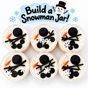 May include: Six clear jars filled with white material, each containing a black top hat, an orange carrot-shaped nose, black sticks for arms, black buttons, and white snowflake decorations. A sign above reads Build a Snowman Jar!