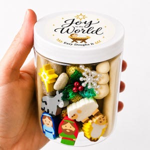 May include: A clear plastic jar with a white lid featuring a label that reads Joy to the World Easy Doughs It. Inside are various small items including a yellow star, a gray donkey, a white sheep, and figures of Mary and Joseph.