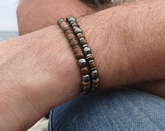 Peut inclure: Deux bracelets empilés sur le poignet d'une personne. Le bracelet du haut est fait de perles de bois brun et le bracelet du bas est fait de perles noires et argentées.