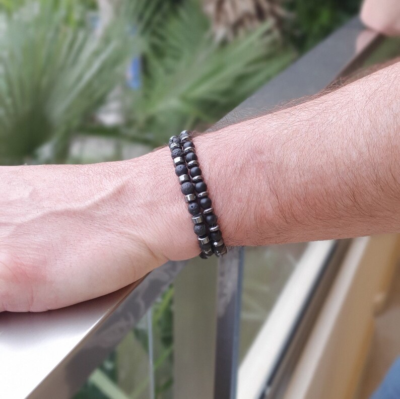 Peut inclure: Deux bracelets sur un poignet. Un bracelet est fait de perles de lave noire et l'autre de perles en m&eacute;tal argent&eacute;.