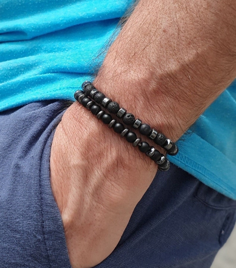 Peut inclure: Deux bracelets en perles noires superpos&eacute;s sur un poignet. Un bracelet est compos&eacute; de perles de lave noire et l'autre de perles d'h&eacute;matite noire.