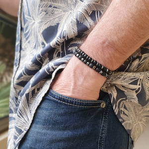 Peut inclure: Un homme portant une chemise &agrave; motifs noir et blanc avec un bracelet en perles noires au poignet.