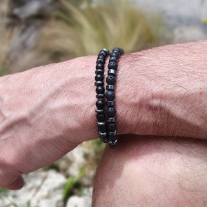 Peut inclure: Deux bracelets en perles sur le poignet d'une personne. Un bracelet est fait de perles de lave noire et l'autre de perles d'onyx noir.