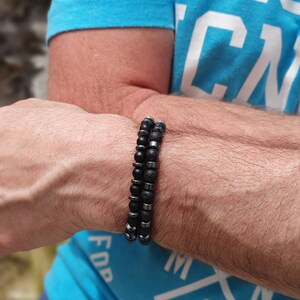 Peut inclure: Deux bracelets en perles sur le poignet d'une personne. Un bracelet est noir avec des perles argent&eacute;es, et l'autre est noir avec des perles grises.
