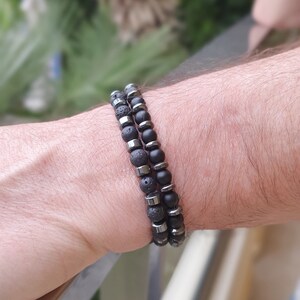 Peut inclure: Deux bracelets en perles noires superpos&eacute;s sur un poignet. Un bracelet est compos&eacute; de perles de lave noire et l'autre de perles d'onyx noir avec des accents argent&eacute;s.