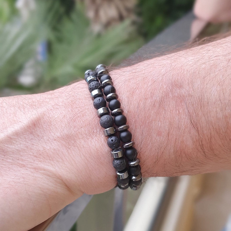 Peut inclure: Deux bracelets en perles noires superpos&eacute;s sur un poignet. Un bracelet est compos&eacute; de perles de lave noire et l'autre de perles d'onyx noir avec des accents argent&eacute;s.