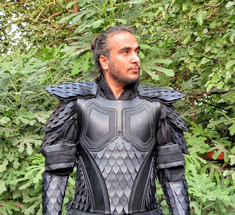 Puede incluir: Una armadura de cuero negro con un patr&oacute;n de escamas. La armadura tiene una pieza de pecho, hombreras y protectores de brazos. La armadura la lleva puesta una persona con el pelo largo y oscuro.
