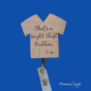Könnte beinhalten: Ein hölzerner Badgehalter in Form eines OP-Kittels mit dem Text "That's a Night Shift Problem" und einem Herzschlag-Symbol. Der Halter ist an einer schwarzen, einziehbaren Badge-Rolle befestigt.