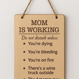 Może przedstawiać: Prostokątny drewniany znak z zaokrąglonymi rogami i sznurkiem do zawieszenia. Wyświetla "MOM IS WORKING" i listę humorystycznych wyjątków. Tekst jest w kolorze ciemnobrązowym. Zabawny element wystroju.