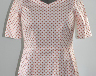 Puede incluir: Un vestido blanco con un patrón geométrico rojo y blanco. El vestido tiene cuello en V, mangas cortas y una falda acampanada.