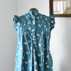 May include: A teal blue dress with a white daisy print and ruffled sleeves. The dress has a button-up front and a fitted bodice.