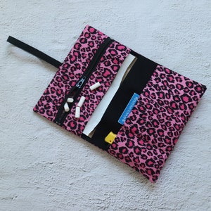 Könnte beinhalten: Eine rosa und schwarze Tasche mit Leopardenmuster und Reißverschluss. Die Tasche ist offen und enthält ein weißes Papier mit einer blauen Karte, auf der "Rolling Papers" steht.