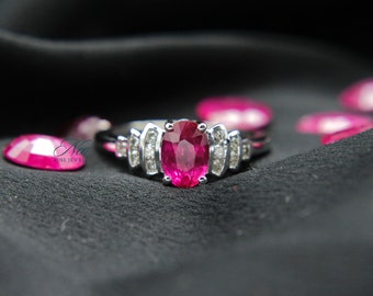 May include: A silver ring featuring a large oval pink gemstone, surrounded by smaller white gemstones. The ring is displayed on a black fabric background.