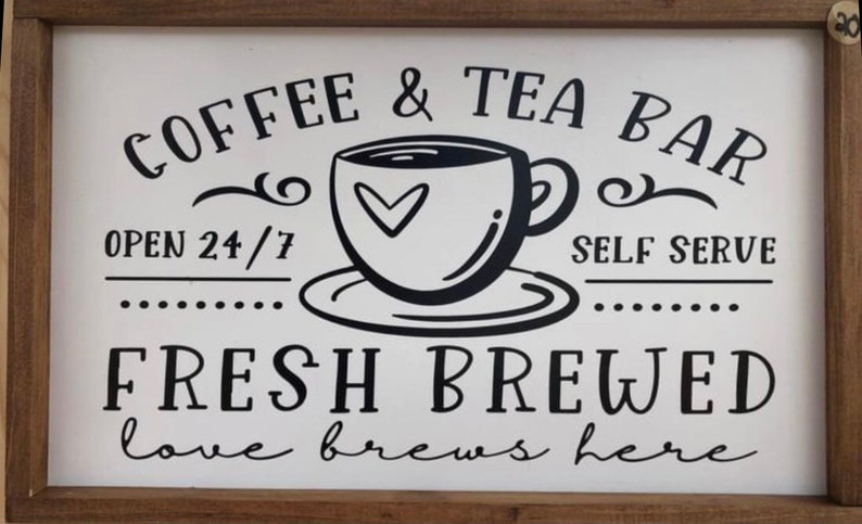 May include: A white sign with black text and a black and white illustration of a coffee cup. The sign reads "Coffee & Tea Bar, Open 24/7, Self Serve, Fresh Brewed, Love brews here."