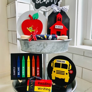 May include: A tiered tray with back-to-school decorations. Features a chalkboard sign, a red apple, a schoolhouse, a crayon sign, a school bus, and stacked books labelled "Reading", "Writing", and "Math".