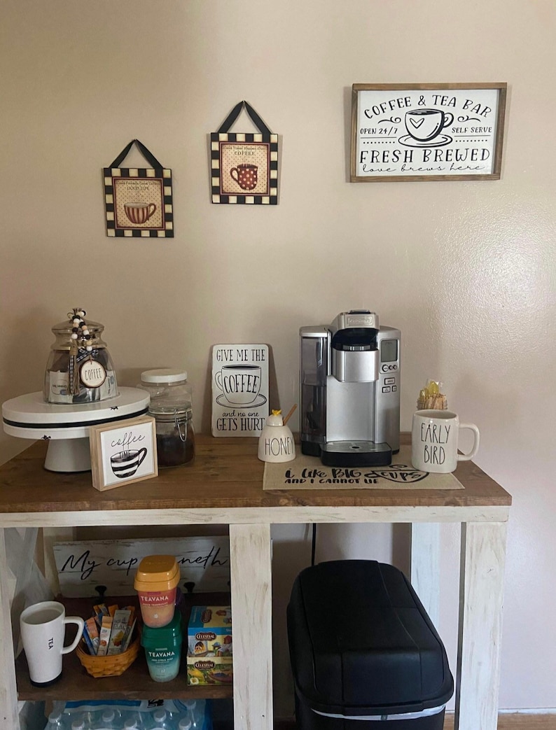 May include: A white wooden coffee bar with a coffee maker, coffee mugs, and a variety of coffee and tea supplies. The bar has a sign that says "Coffee & Tea Bar" and "Fresh Brewed Love Brews Here".