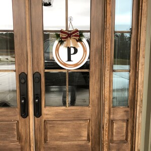 May include: A wooden front door with a glass panel featuring a wreath with a burlap bow and the letter "P" in the center.