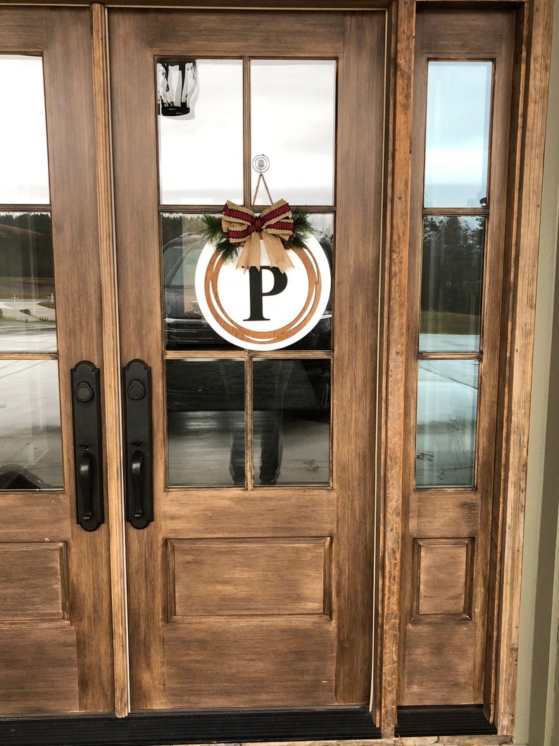 May include: A wooden front door with a glass panel featuring a wreath with a burlap bow and the letter "P" in the center.