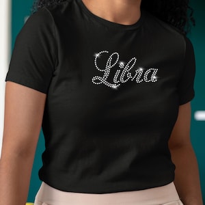 Könnte beinhalten: Schwarzes T-Shirt mit dem Wort "Libra" in Strasssteinen.